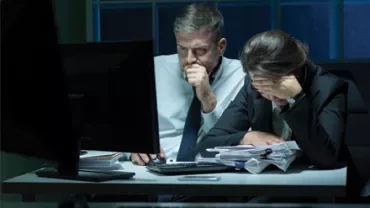 Deux personnes travaillant tard dans un bureau, regardant un écran d'ordinateur avec concentration.