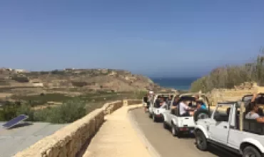Caravan de voitures blanches sur une route côtière avec vue sur la mer.